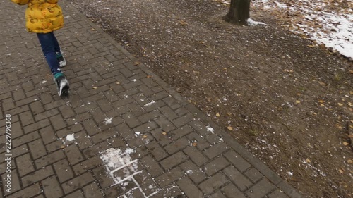 Little girl in yellow jacket brings snow in winter city park.