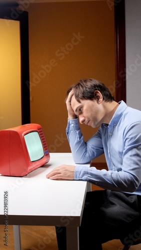 Fotografie Man resting his forehead in one hand and staring at a vintage red television, co