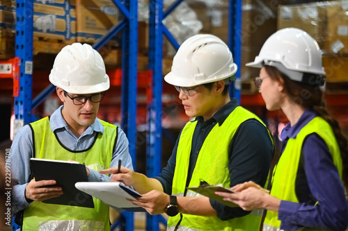 Three Construction Workers Collaborating in a Warehouse with Safety Gear, Taking Notes and Analyzing Inventory Data for Efficient Operations