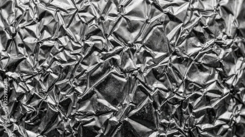 Crinkled aluminum foil texture with sharp metallic ridges and deep shadows creating a high contrast monochrome abstract pattern for modern industrial background or creative graphic design projects