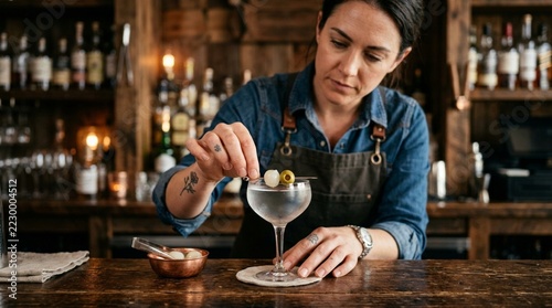 Bartender Garnishing Martini Cocktail with Olives in Moody Bar Setting