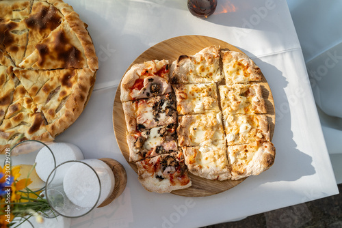 Top view of sliced pinsa pizza on wooden platter at garden table