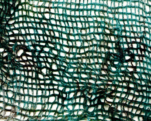Texture of worn, dark-indigo mesh fabric, featuring stains and an uneven surface. Close-up view of a crumpled, soiled piece of gauze.
