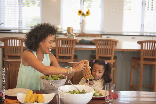 African American mother serving salad to her daughter at dining table