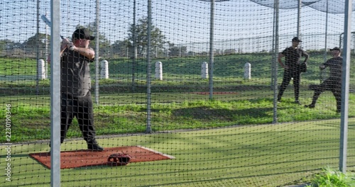 Diverse males capped practicing in park batting cage, batter on orange mat holding bat, copy space