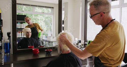 Focused caucasian male hairdresser styling bleached hair of happy female client at salon