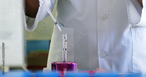 A scientist in a lab coat is pipetting a liquid into a test tube, with copy space