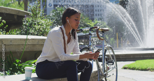 African american woman with bike using smartphone wearing earphones in city park