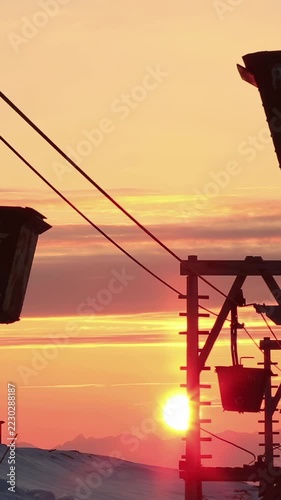 An old abandoned coal cableway with rusted buckets suspended against a golden sunset and snow-covered mountains in Longyearbyen town Svalbard Norway