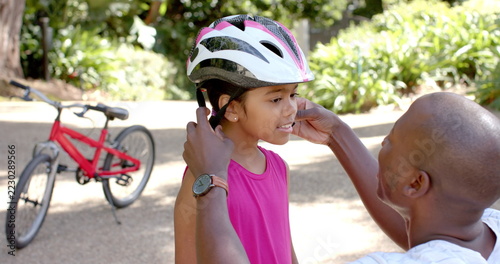 Adjusting bike helmet, father ensuring daughter's safety before cycling outdoors