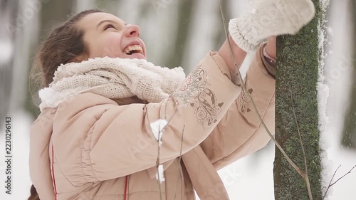 Slow motion. Teen girl shakes a young tree from snow in a winter park.