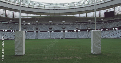 Goal posts on rugby pitch at empty sports stadium with tiered seating, copy space