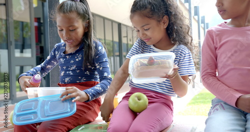 In school, three children sitting with lunchboxes and apple during break