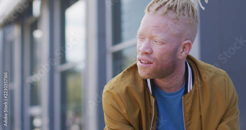 Thoughtful albino african american man with dreadlocks on bike using smartphone