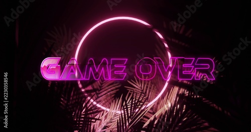 Glowing GAME OVER sign and circular neon ring dominating dark studio set, with palm fronds