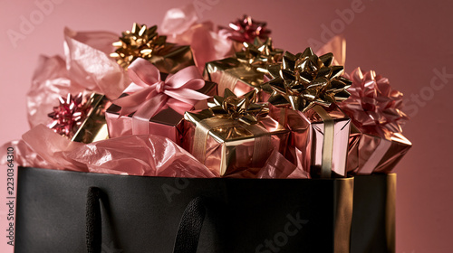 Black Shopping Bag Overflowing with Gifts on Pink Background, Shopping Spree Concept