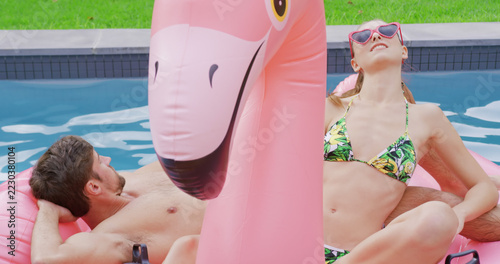 Happy caucasian couple relaxing on inflatables in swimming pool in garden
