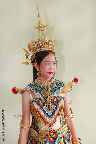 Fotografie A young Asian girl wearing a traditional southern Thai Manohra costume and elaborate golden crown, smiling gently while posing for a cultural dance performance