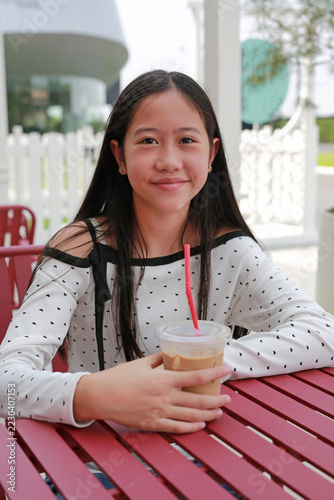A young Asian girl enjoying her iced latte at a charming outdoor cafe.