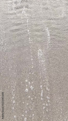 White sea wave foam rushing onto sandy beach during summer