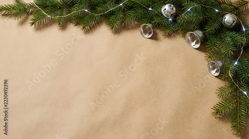 Green pine branch with silver bells and lights on beige paper background