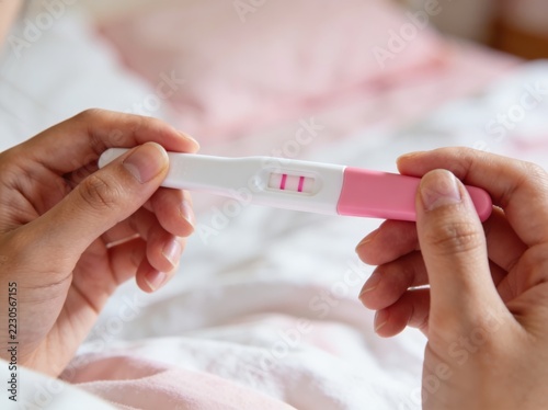 Hands holding positive pregnancy test with two visible lines on pink strip