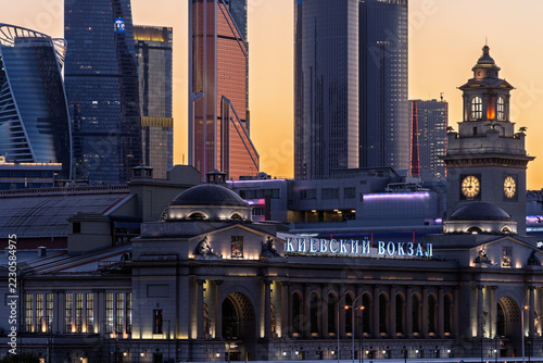 Moscow Kievsky railway station beneath modern skyscrapers at sunset. Historic transport hub and contemporary city architecture. Urban travel, rail infrastructure and metropolitan skyline.
