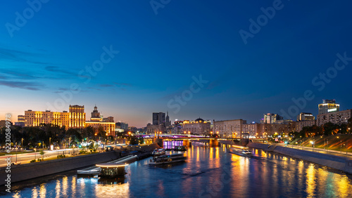 Moscow city skyline along the Moskva River at twilight. Illuminated bridges and riverside buildings reflected in the water. Urban travel destination. Evening cityscape and waterfront