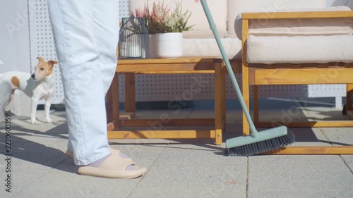Person sweeping patio tiles with a broom near outdoor furniture. Outdoor housework and terrace maintenance