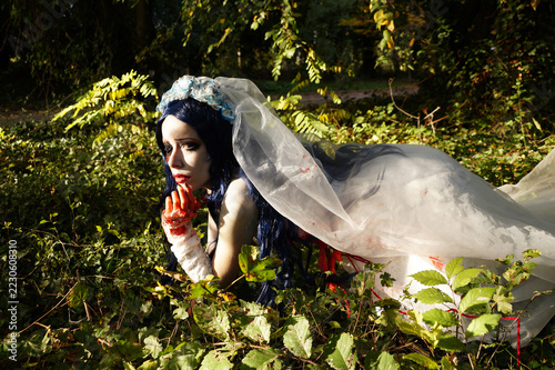 dead bride in white wedding dress and veil lying in forest, bloody hand, spooky halloween