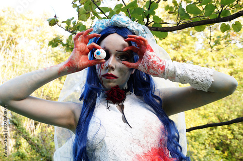 halloween bride holding fake eyeball in bloody hands, blue hair and black eye makeup, creepy horror portrait