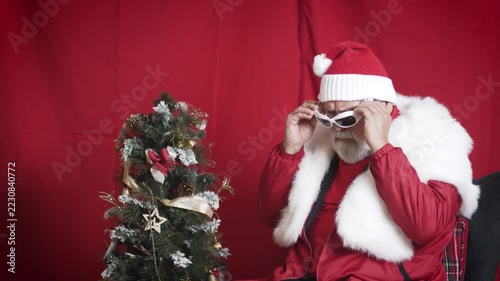 Santa puts on sunglasses, poses, then leaves beside small tree