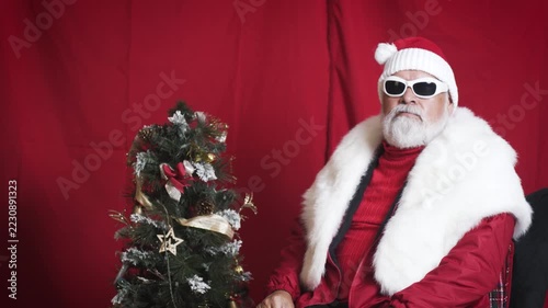 Cool Santa puts on white sunglasses beside small Christmas tree