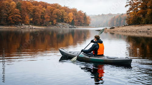 Kayaker paddling on a lake surrounded by autumn forest. Man canoeing on water with fall foliage reflections