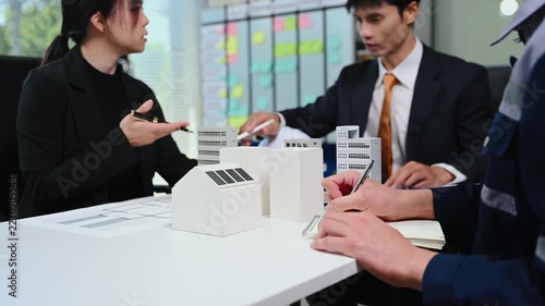 Professional engineers and architects discussing urban development and construction projects with building models and blueprints in a modern office.