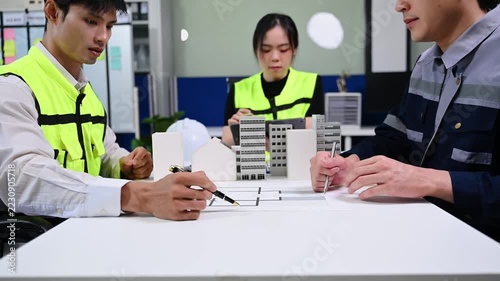 Professional engineers and architects discussing urban development and construction projects with building models and blueprints in a modern office.