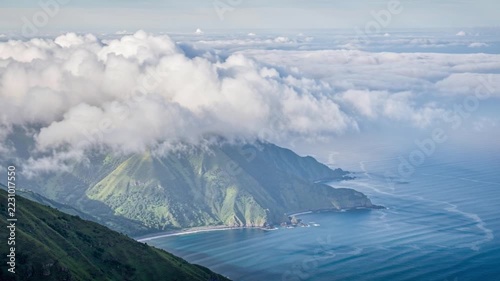 Clouds rolling over a lush green coastal mountains slope by the sea