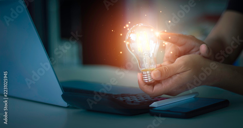 Hands holding bright glowing light bulb with sparkle light effect for business innovation, new idea, and solution concept.