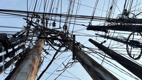 Dense canopy of disorganized electrical wires and communication cables silhouetted against a bright sky demonstrating urban sprawl and the challenging complexity of overhead city infrastructure.