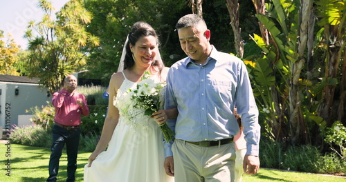 Happy diverse senior bride and groom walking arm in arm and embracing with diverse senior friends at