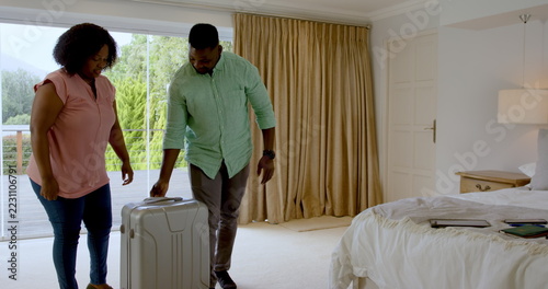 African American couple embracing joyfully in bedroom with suitcase nearby