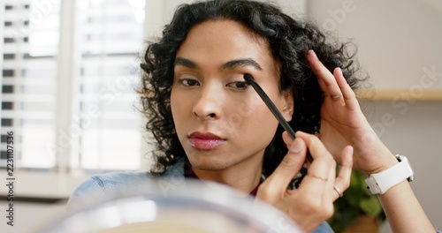 Holding brush with brown eyeshadow, nonbinary person blending crease for symmetry at vanity mirror