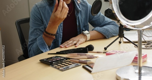Non-binary creator showing red lip gloss shade before demoing powder brush usage tip at home studio