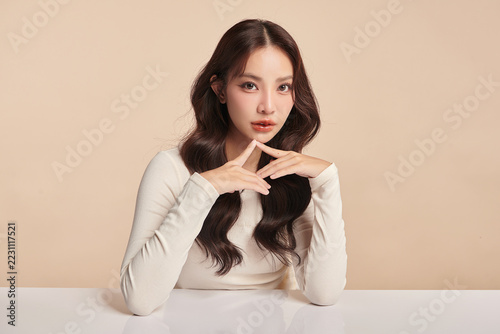 A beautiful young Asian woman with clean, fresh skin against a beige background. Skincare, facial treatment, cosmetology, beauty, and spa. An elegant portrait of an Asian woman.