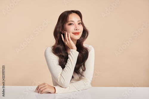 A beautiful young Asian woman with clean, fresh skin against a beige background. Skincare, facial treatment, cosmetology, beauty, and spa. An elegant portrait of an Asian woman.