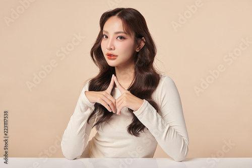 A beautiful young Asian woman with clean, fresh skin against a beige background. Skincare, facial treatment, cosmetology, beauty, and spa. An elegant portrait of an Asian woman.