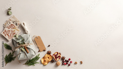 Rustic Christmas Present Wrapped in Sage Green Linen with Jute Twine, Eucalyptus and Cinnamon, Surrounded by Dried Fruit, Evergreen Sprigs and Recycled Craft Paper