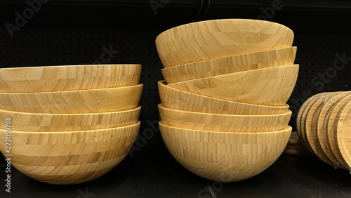 Stacks of wooden bowls stand on dark display shelf in retail store. This closeup shot illustrates sustainable lifestyle and natural minimalism.