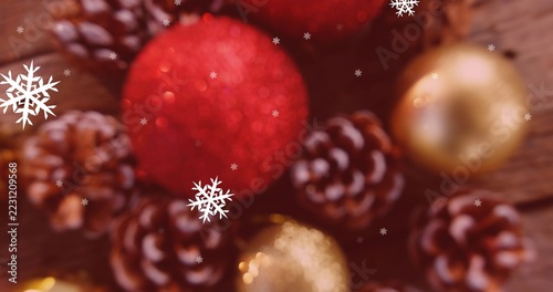 Glittering red glitter bauble dominating wooden tabletop, surrounding pine cones and gold baubles