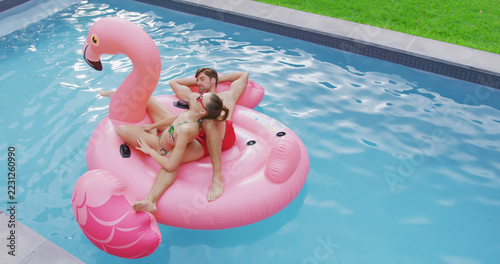 Happy caucasian couple relaxing on inflatables in swimming pool in garden